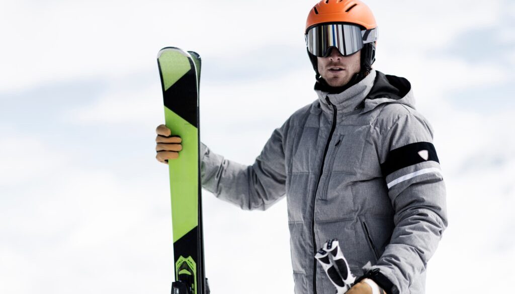 Man wearing helmet and ski goggles holding skis, portrait