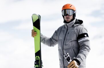 Man wearing helmet and ski goggles holding skis, portrait